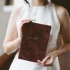bride holding wedding story writer burgundy wine gold vow book Asian elopement in CA