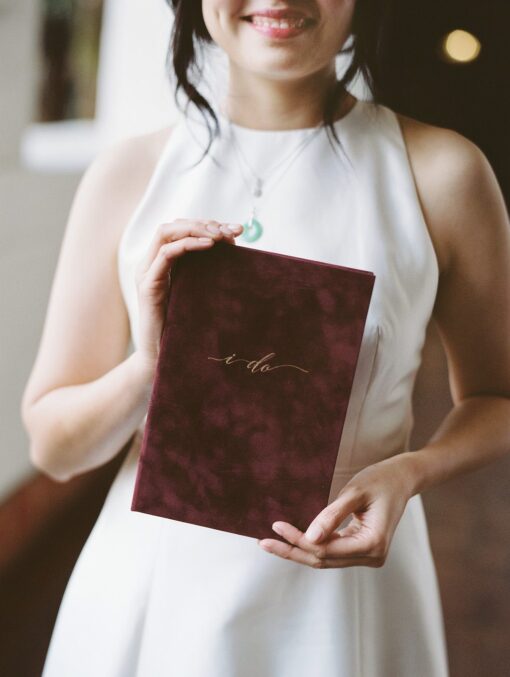 bride holding wedding story writer burgundy wine gold vow book Asian elopement in CA