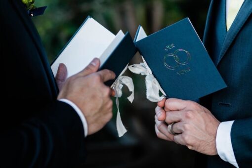 two grooms holding Our Vows vow books in rainbow foil
